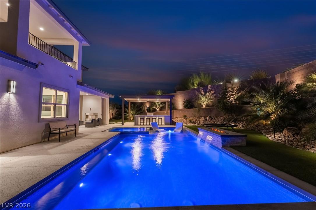 127 Malpaso St resort backyard, pool and fire feature illuminated at night in Summerlin West, Las Vegas